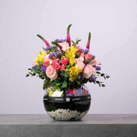 Vibrant round floral arrangement with pink, yellow, and purple flowers in a BLUMEN glass bowl.