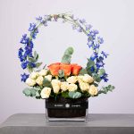 Vibrant floral arrangement of pink and purple flowers in a square glass vase.