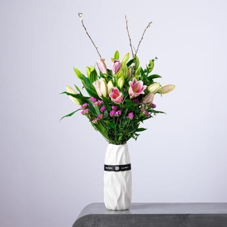 Elegant arrangement of pink lilies and purple flowers in a white textured vase.