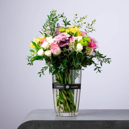 Fresh mixed flower arrangement with roses, chrysanthemums, and greens in a tall BLUMEN vase.