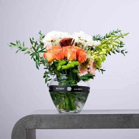 Fresh orange and white flower arrangement with roses and greenery in a BLUMEN glass vase.