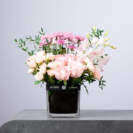 Soft pastel flower arrangement with pink roses, spray roses, and chrysanthemums in a BLUMEN vase.