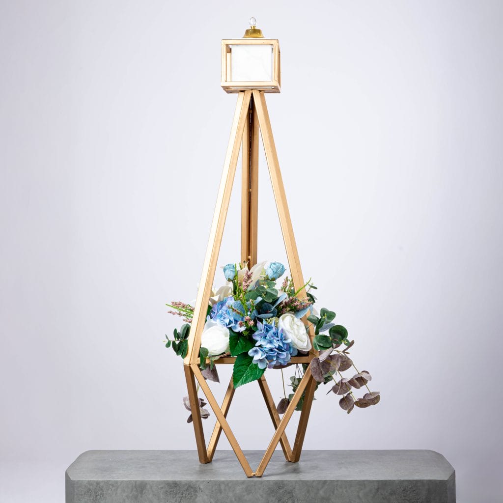 Modern floral arrangement with blue hydrangeas and white roses in a tall golden geometric frame.