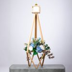 Modern floral arrangement with blue hydrangeas and white roses in a tall golden geometric frame.