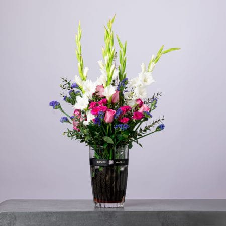 Tall floral arrangement with white, pink, and purple blooms in a BLUMEN vase.
