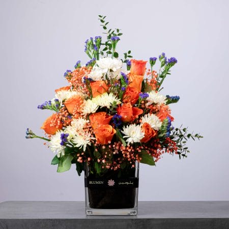 Bright floral arrangement with orange roses, white chrysanthemums, and blue statice.