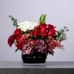Elegant arrangement of pink roses and orchids in a square glass vase with a purple BLUMEN ribbon.