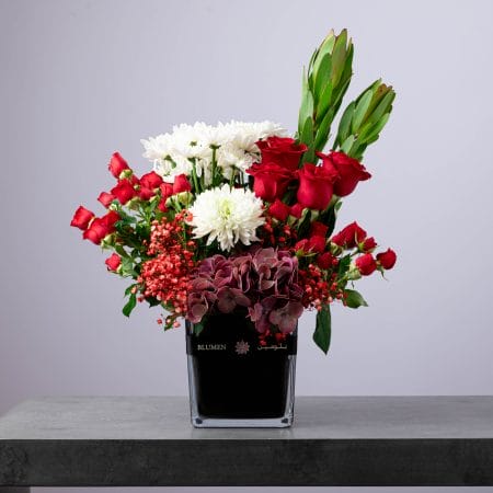 Luxurious red and white flower arrangement with roses, chrysanthemums, and hydrangeas in a black BLUMEN vase.