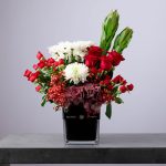 Elegant floral arrangement with red roses, white chrysanthemums, and burgundy hydrangeas in a black glass vase.