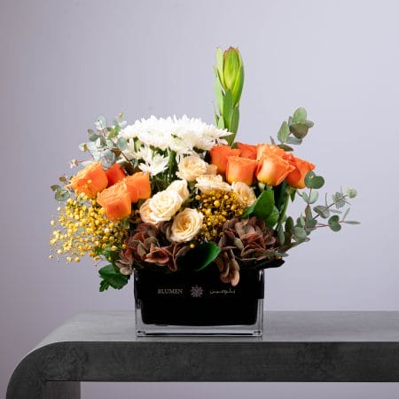 Elegant floral arrangement with orange and cream roses, white chrysanthemums, and eucalyptus in a black glass vase.