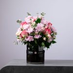 Elegant bouquet of pink chrysanthemums and two-tone roses arranged in a round glass vase.