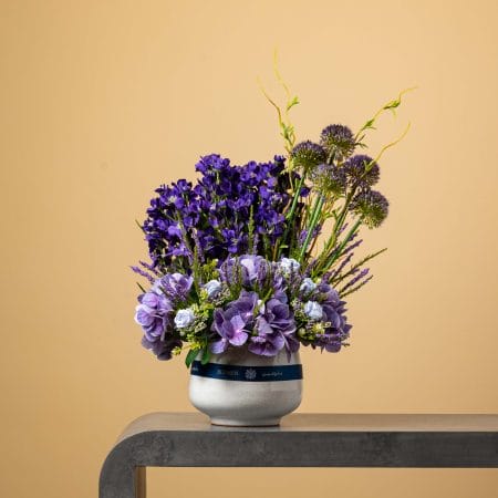 Artificial purple floral arrangement in a stone-textured vase.