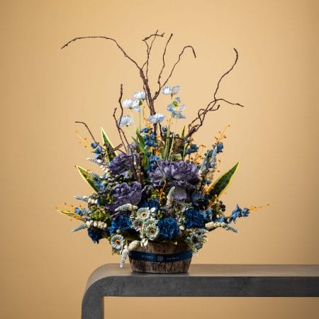 Artificial blue and gray floral arrangement with white highlights in a rustic pot.