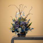 Artificial blue and gray floral arrangement with white highlights in a rustic pot.