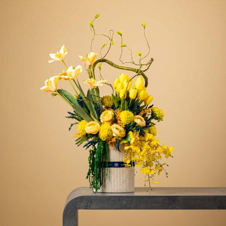 Artificial yellow tulip and orchid arrangement with curly branches in a tall ribbed vase.