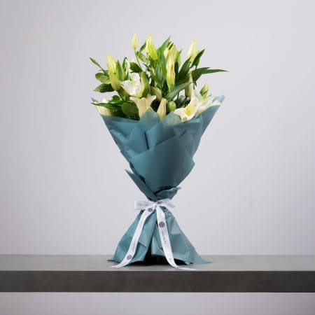 White lily bouquet wrapped in teal paper with white ribbon.