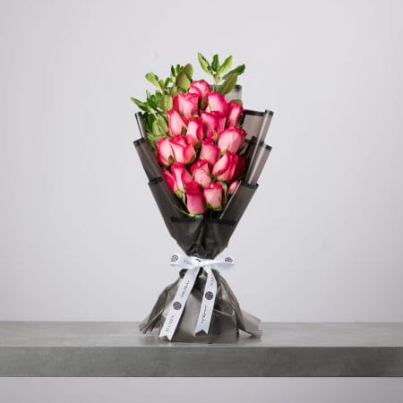 Pink rose bouquet wrapped in smoky black paper with white ribbon.