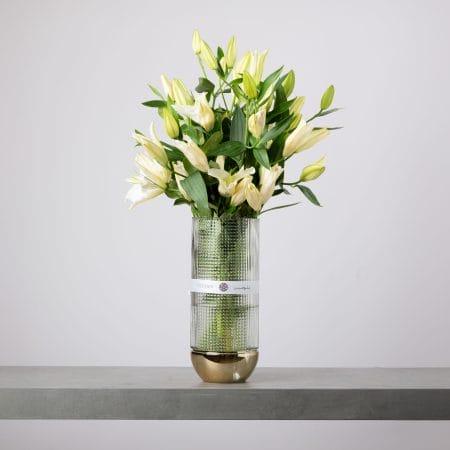White lily arrangement in tall glass vase with gold base.