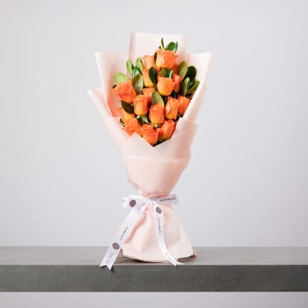 باقة ورود برتقالية أنيقة ملفوفة بورق وردي فاتح من بلومن