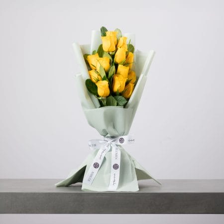 Yellow rose bouquet wrapped in soft green paper with white ribbon.