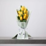 Yellow rose bouquet wrapped in soft green paper with white ribbon.