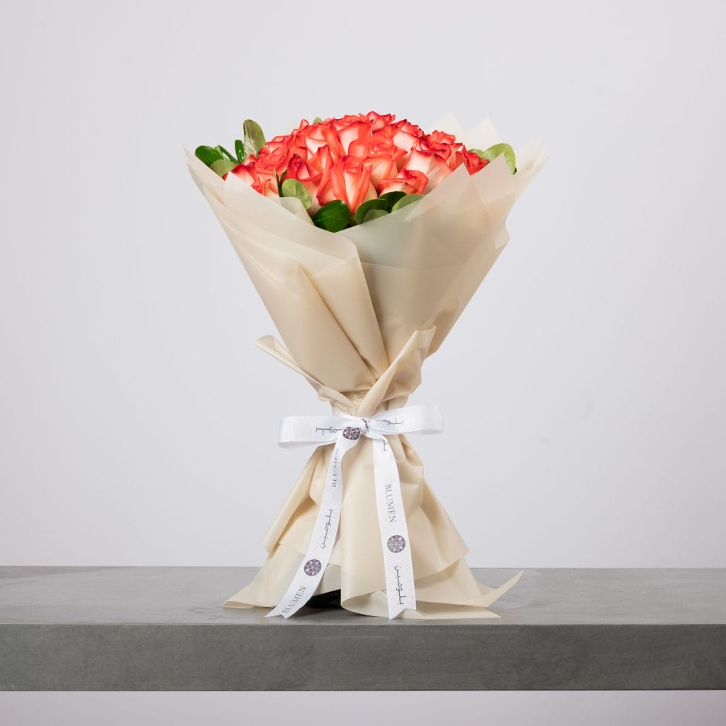 Coral-hued roses bouquet wrapped in soft beige paper