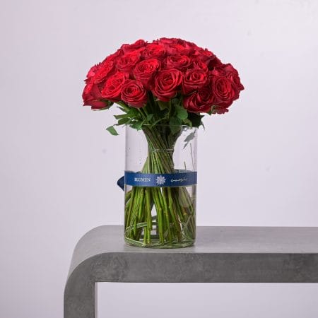 Luxurious bouquet of red roses in a tall BLUMEN glass vase.