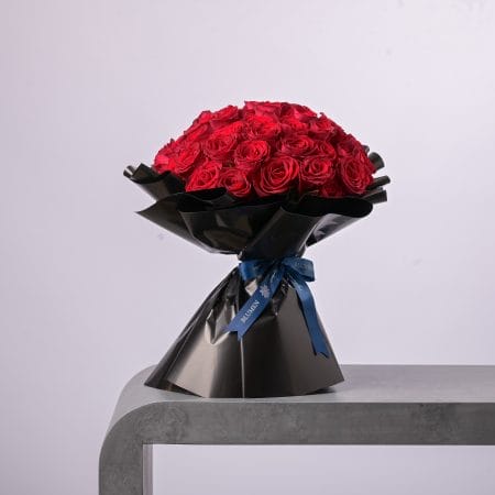 Elegant black-wrapped bouquet of red roses tied with a blue BLUMEN ribbon.