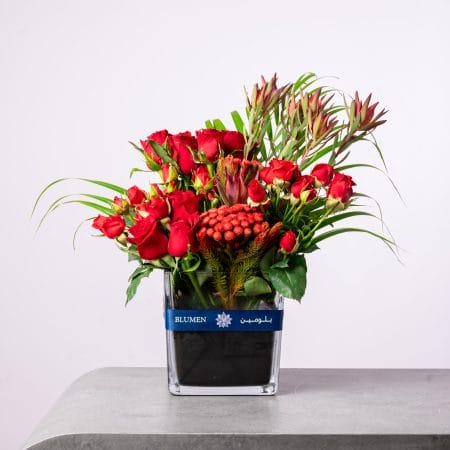 Red floral arrangement with roses and exotic textures in a BLUMEN square vase.
