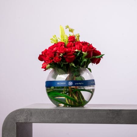 Artistic floral arrangement with yellow roses and purple accents in a black glass vase.