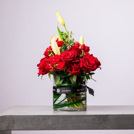 Elegant arrangement of red roses and lilies in a round BLUMEN vase.
