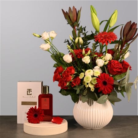 Floral arrangement with red roses, red gerberas, ivory flowers, and greenery in a rounded textured vase.