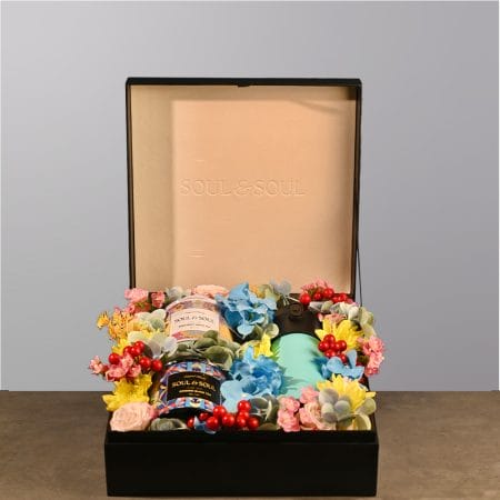 Gift box featuring two tea tins and a thermos surrounded by colorful floral arrangement.