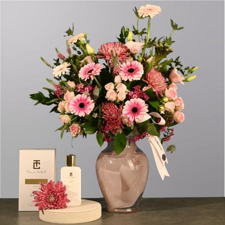 Pink floral arrangement with gerberas, spray roses, and greenery in a soft pink glass vase wrapped with fabric.