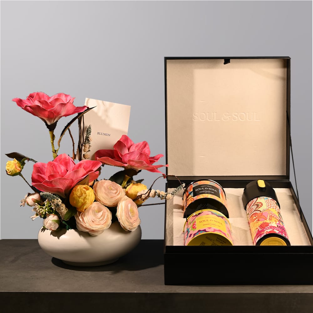 Floral arrangement with peach and red-pink roses in a short, wide white elliptical vase.