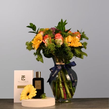 Floral arrangement with yellow blooms, peach roses, and greenery in a clear rounded glass vase.