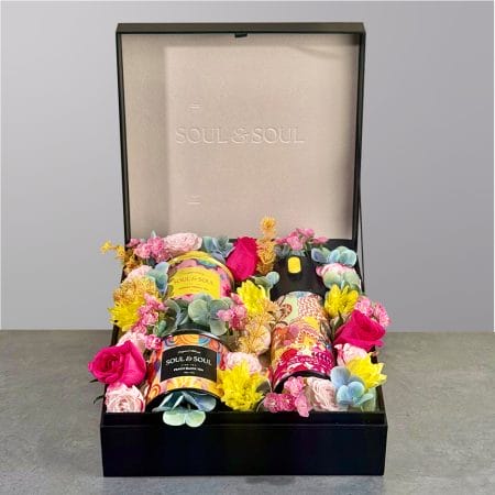 Gift box featuring two tea tins and a thermos surrounded by colorful floral arrangement.