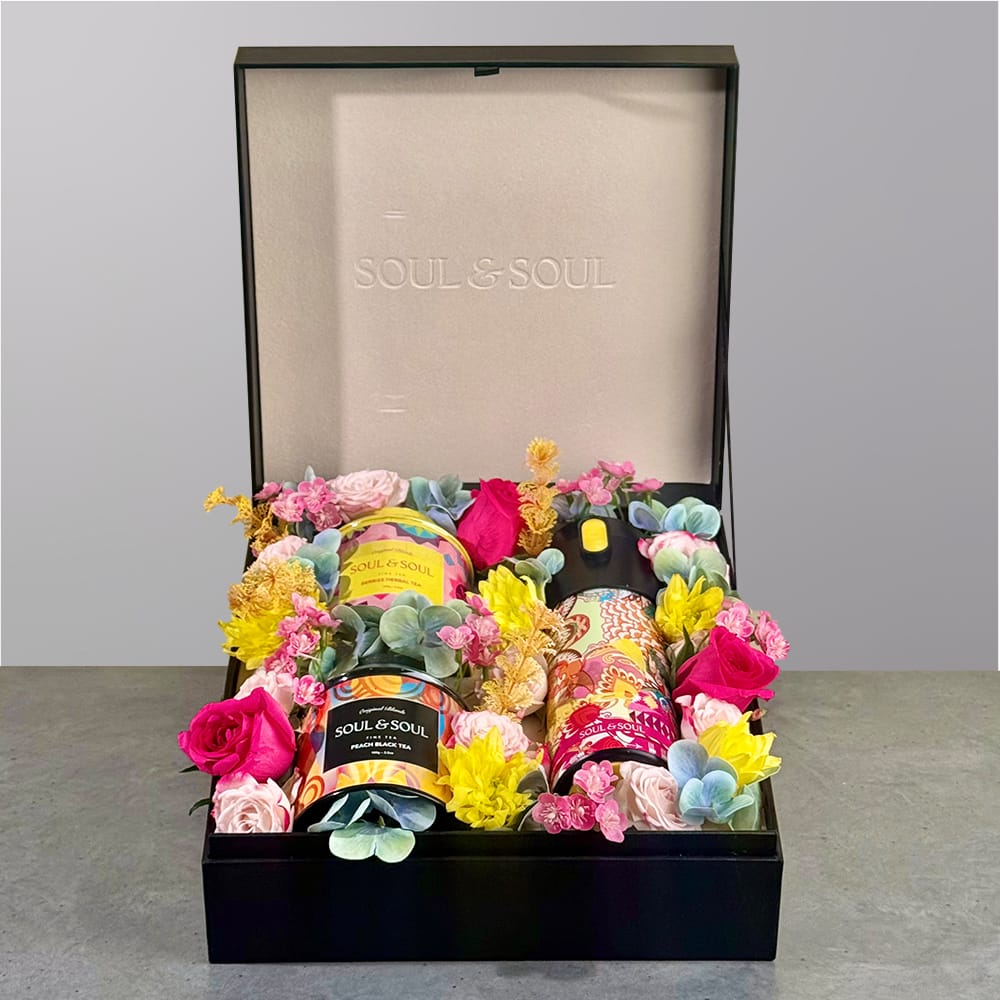 Gift box featuring two tea tins and a thermos surrounded by colorful floral arrangement.