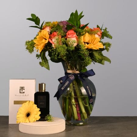 Floral arrangement with yellow blooms, peach roses, and greenery in a clear rounded glass vase.