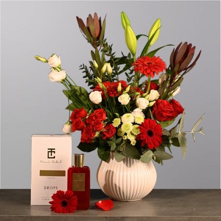Floral arrangement with red roses, red gerberas, ivory flowers, and greenery in a rounded textured vase.