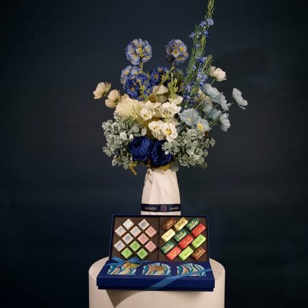 تنسيق أزهار أنيق يضم أزهارًا بدرجات الأزرق الداكن والعاجي والأزرق الفاتح مع خضرة غنية داخل مزهرية خزفية بتصميم فني.