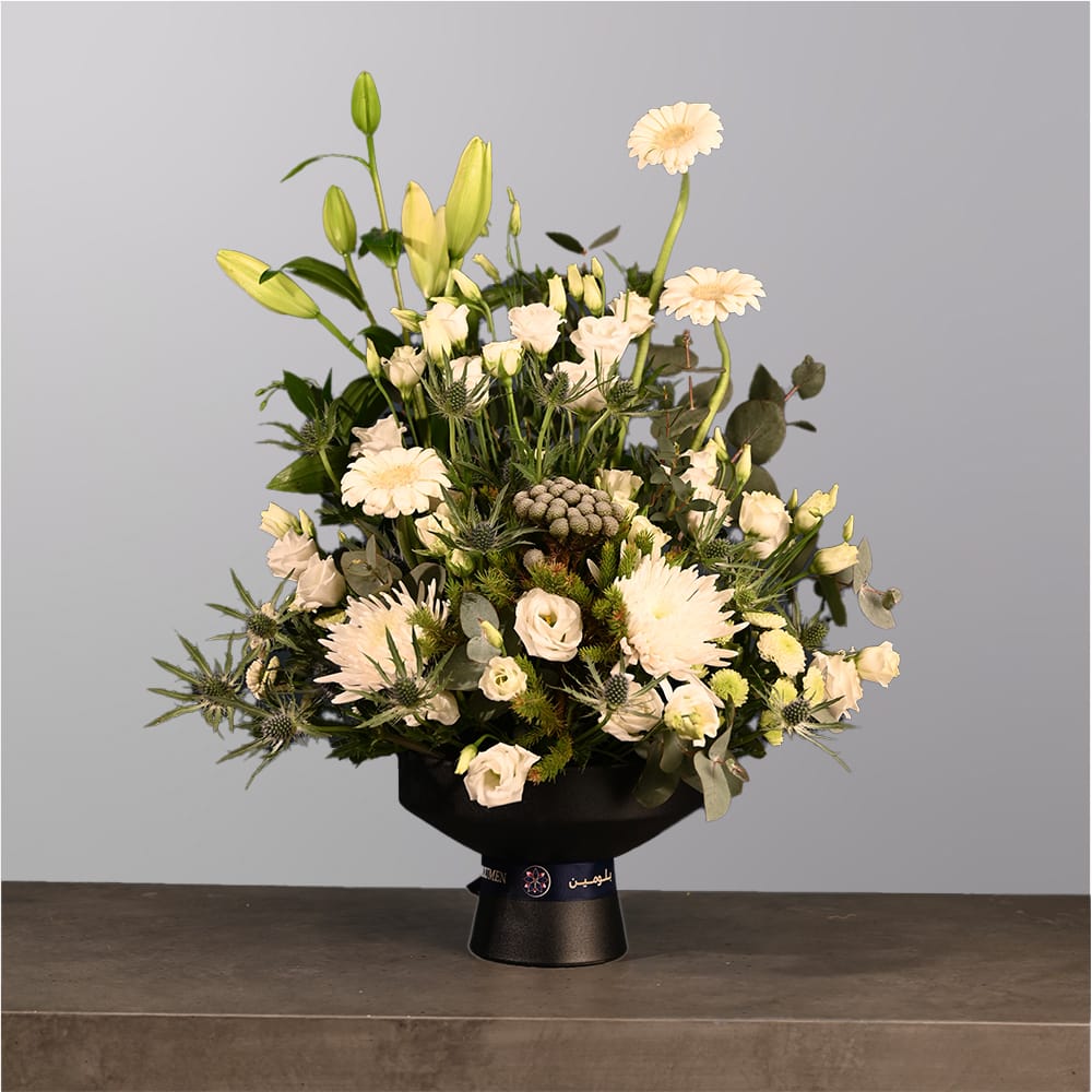 A sophisticated arrangement of white flowers including lilies, roses, and gerberas with greenery, displayed in a matte black vase.