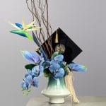 A modern floral arrangement featuring blue orchids, tropical flowers, sculptural branches, and greenery in a ceramic vase with artistic styling.