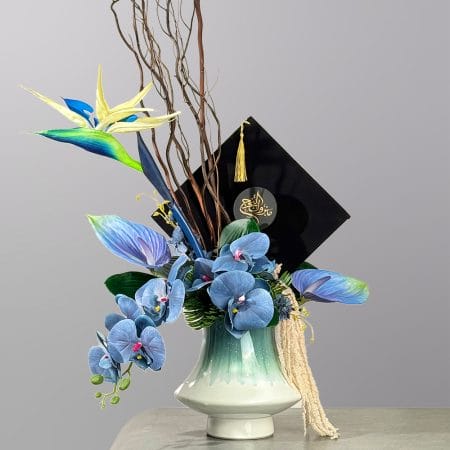 A modern floral arrangement featuring blue orchids, tropical flowers, sculptural branches, and greenery in a ceramic vase with artistic styling.