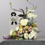 A sophisticated graduation-themed floral arrangement featuring white blooms, blush roses, eucalyptus, and artistic branches beside a congratulatory graduation sign.