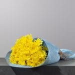 A hand-tied bouquet of vibrant yellow chrysanthemums, wrapped in elegant blue fabric and finished with a natural twine accent.