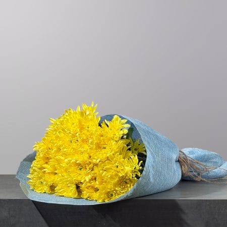 A hand-tied bouquet of vibrant yellow chrysanthemums, wrapped in elegant blue fabric and finished with a natural twine accent.
