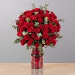 A luxurious floral arrangement featuring premium red roses, white lilies, and seasonal blooms elegantly arranged in a modern decorative vase.