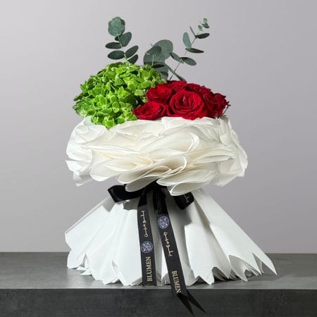 Elegant bouquet featuring green hydrangea, deep red roses, and eucalyptus wrapped in luxurious white paper.