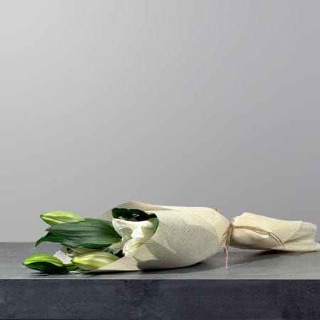The Lily Haven hand-tied bouquet featuring fresh white lilies and lush greenery wrapped in natural beige fabric.